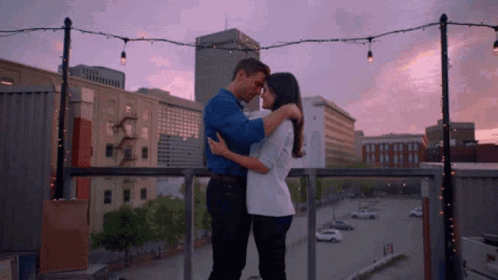 Man And Woman Hugging On Balcony Overlooking City Sunset GIF
