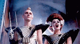 Man And Woman In Futuristic Costumes Holding Trident GIF