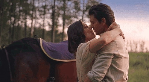 Man and Woman Kissing in Front of a Horse in a Field