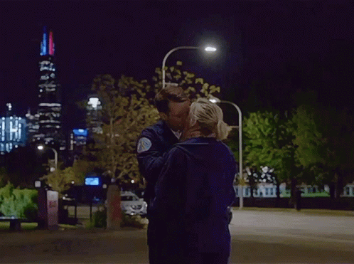 Man and Woman Kissing in Front of City Skyline at Night