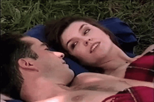 Man And Woman Laying On Blue Pillow In Grass GIF