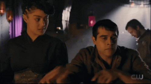 Man And Woman Sitting At Table With CW Logo GIF