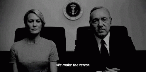 Man and Woman Sitting in Front of Sign Saying We Make The Terror