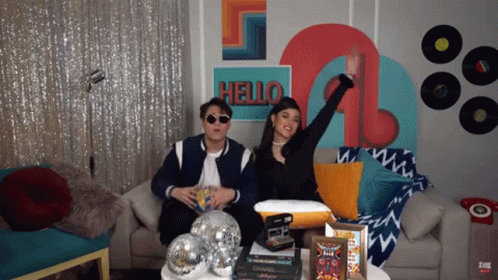 Man And Woman Sitting On Couch Before Hello Wall GIF