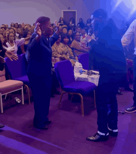 Man And Woman Stand Before Crowd In Purple Chairs GIF