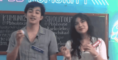 Man And Woman Standing In Front Of Shoutout Sign GIF