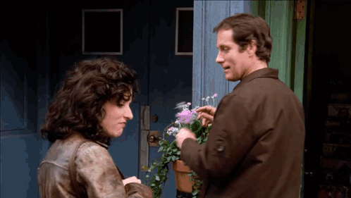 Man And Woman Talking About Flowers In Front Of Blue Door GIF