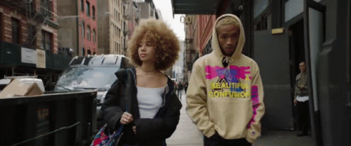 Man and Woman Walking Down Street Wearing Hoodie Saying Reality