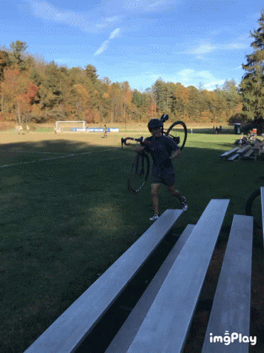 Man Carrying Bike Across Bleacher Field Imgplay GIF