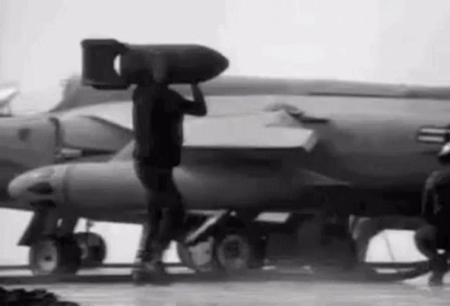 Man Carrying Large Bomb On Head In Front Of Jet GIF