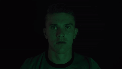 Man Covering Mouth in Dark Room with Green Light
