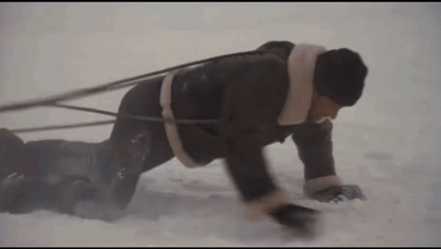 Man Crawling Through Snow Pulling Another Man On Sled GIF