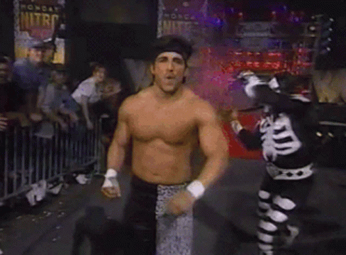 Man Dancing Shirtless in Front of Crowd With Skeleton Behind