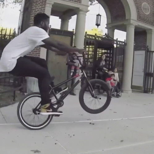 Man Doing Bike Trick In Front Of Brick Building GIF