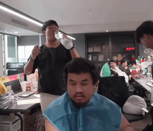 Man Drinking From Bottle While Another Shaves His Head