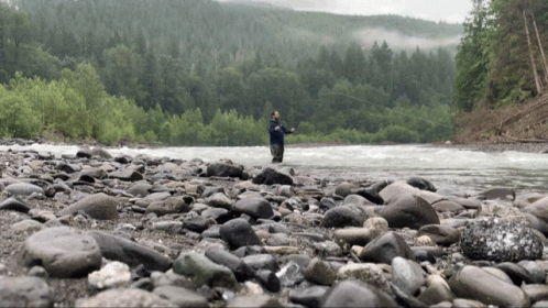 Man Fishing in River Surrounded by Rocks and Trees