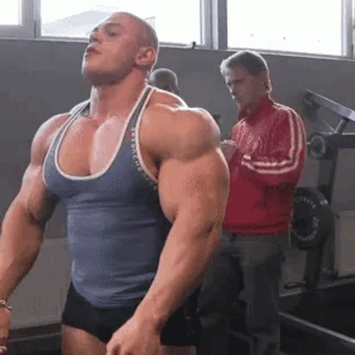 Man Flexing Muscles While Man in Red Jacket Watches