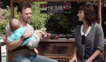 Man Holding Baby in Front of Tikibar