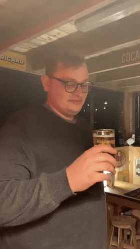 Man Holding Beer in Front of Ricard Sign