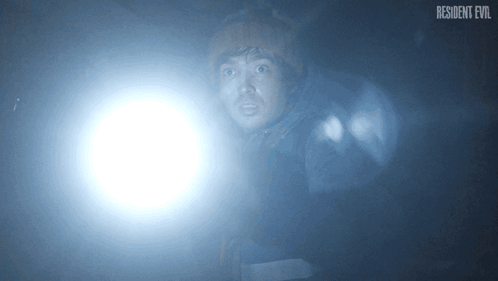 Man Holding Flashlight In Dark Room With Resident Evil Logo GIF