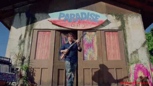Man Holding Gun In Front Of Paradise Gift Shop GIF