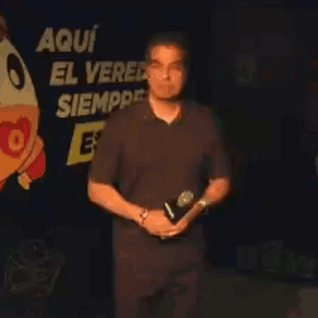 Man Holding Microphone In Front Of Sign Aqui El Ver Siempre GIF