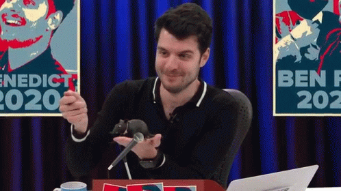 Man Holding Mouse at Microphone at Table With Laptop