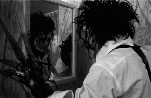 Man Holding Scissors in Front of Mirror