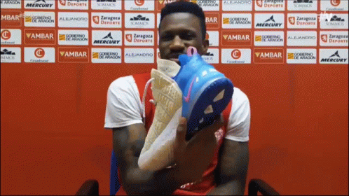 Man Holding Shoes In Front Of Ambar Wall GIF