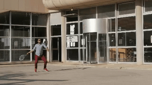 Man Holding Tennis Racquet in Front of Building with A Sign