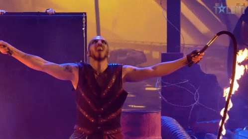 Man Holding Whip In Front Of Fire And BBC Talent Sign GIF