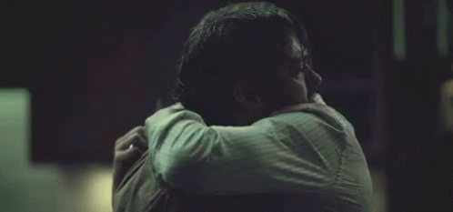 Man Hugging Another Man Holding Head Dark Room