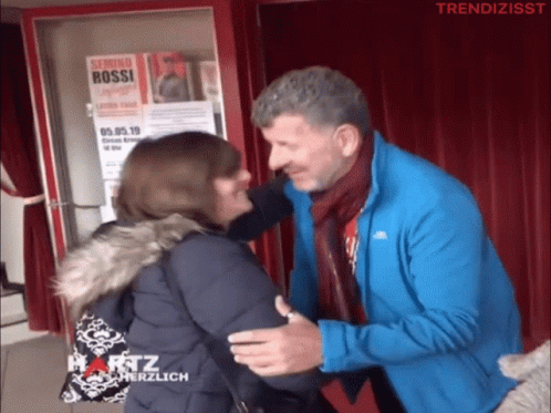 Man Hugging Woman in Front of Serimo Bossi Sign