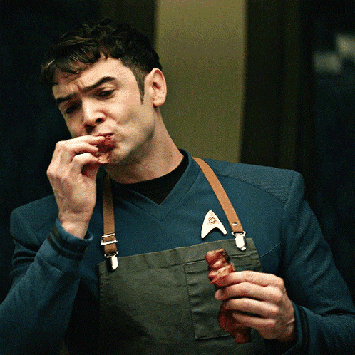Man in Apron and Star Trek Badge Eating Meat