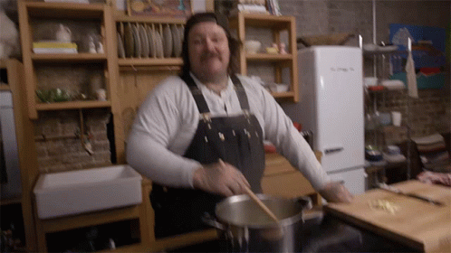 Man in Apron Stirring Pot With Wooden Spoon in Kitchen