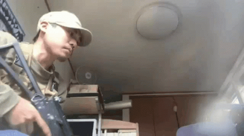 Man In Baseball Cap Holding Gun In Room With Fan GIF