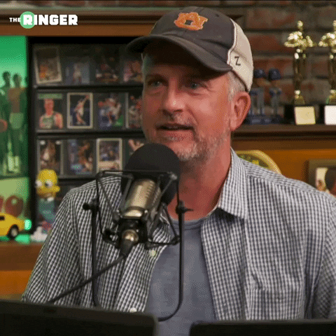 Man in Baseball Cap Talking Into Microphone