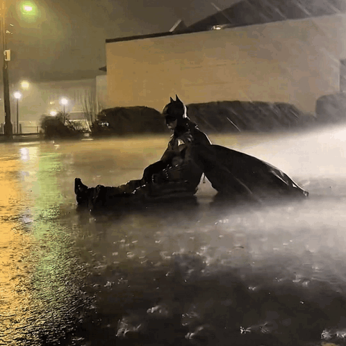 Man in Batman Costume Laying in Rain