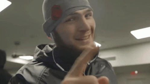 Man In Beanie And Earbuds Smiling Giving Middle Finger GIF