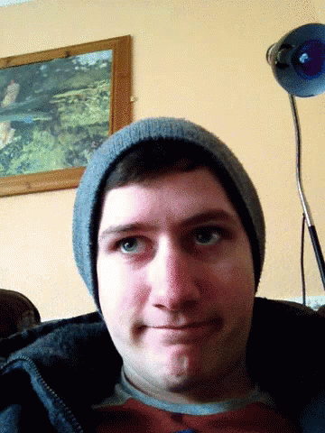 Man in Beanie Looks at Camera With Lamp Behind Him