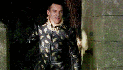 Man in Black and Gold Suit Standing Before Stone Wall