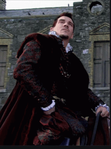 Man in Black and Red Coat in Front of Stone Wall