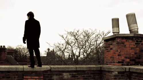 Man In Black Coat Standing On Brick Wall GIF