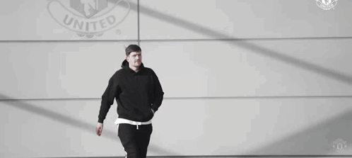 Man in Black Hoodie and Pants Walking in Front of United Logo Wall