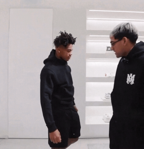 Man in Black Hoodie With Letter M Talks to Another Man