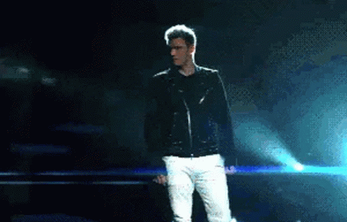 Man in Black Jacket and White Pants on Stage Holding Microphone