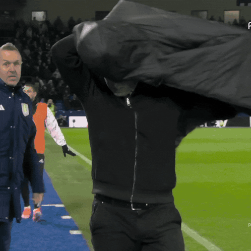 Man in Black Jacket Holding Bag Over Head on Soccer Field