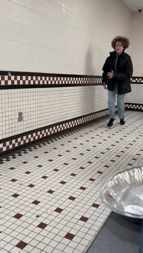 Man in Black Jacket Walking Down Tiled Hallway