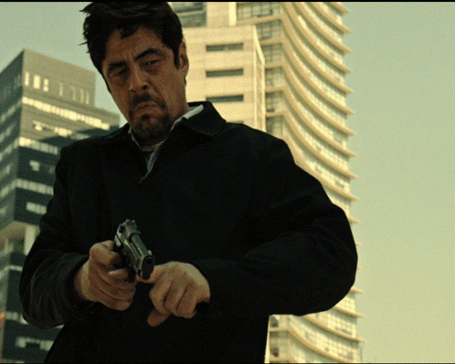 Man in Black Jacket with Gun before Tall Buildings
