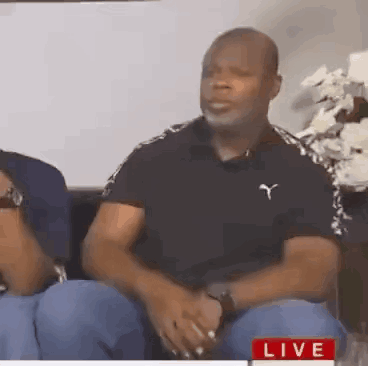 Man In Black Puma Shirt Sitting On Couch Talking To Another Man GIF